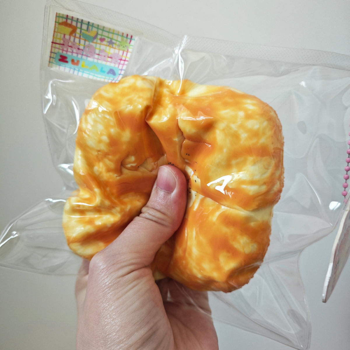 A hand holding a packaged yellow-orange bread-shaped squishy toy against a plain light background.
