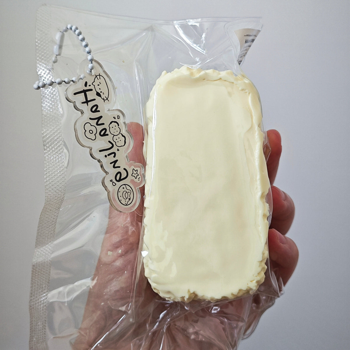 A hand holding a packaged cream-colored rectangular item in clear plastic packaging with a decorative tag that reads 'HongJing'.