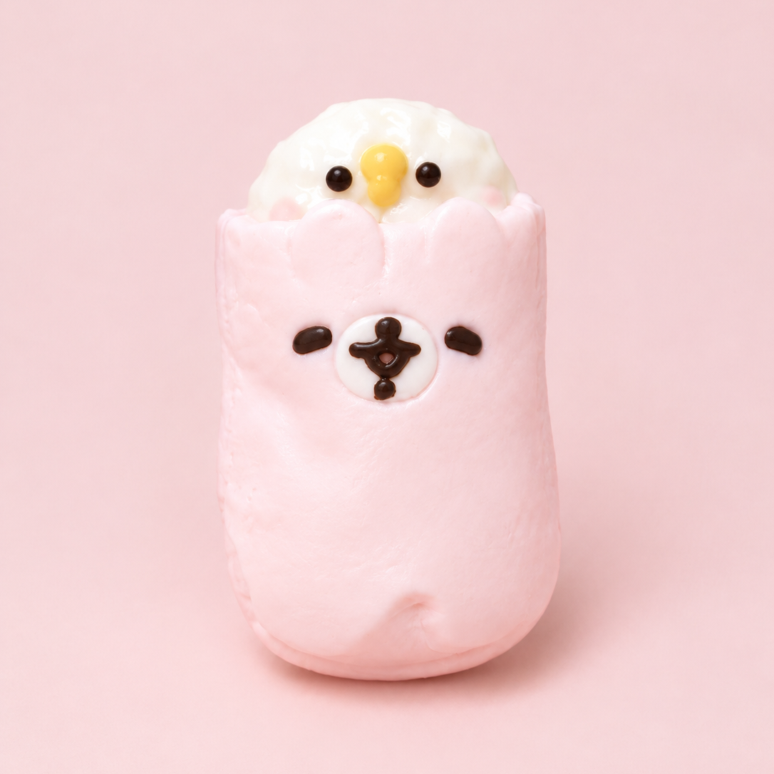 A cute, soft squishy toy shaped like a wrapped snack or character, featuring a pink body, a white top section, small black facial details, and a tiny yellow beak, set against a solid light pink background.