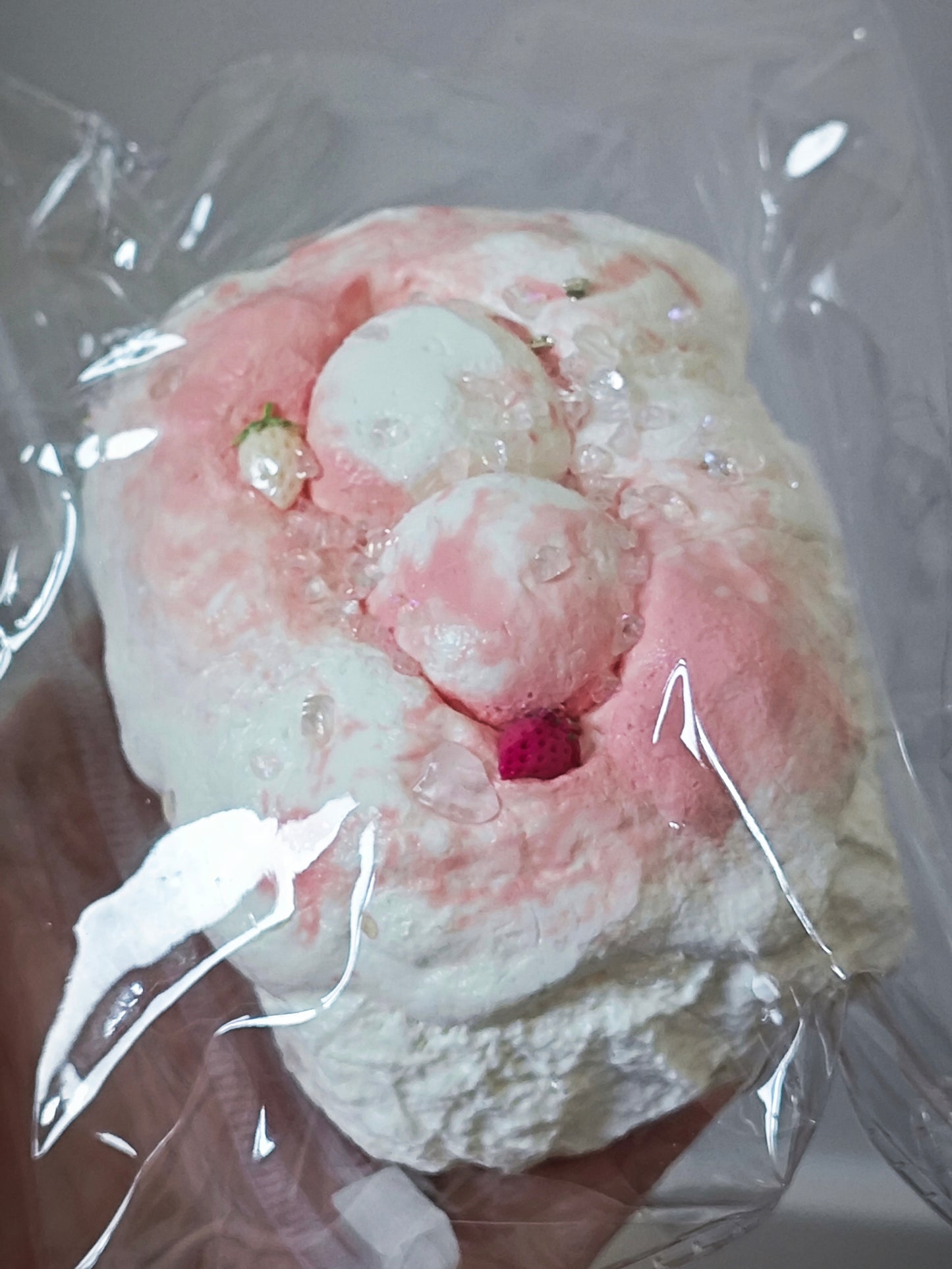 A close-up of a pink and white textured foam or sponge-like product wrapped in clear plastic, held in a hand.