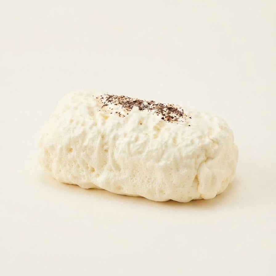 A single white, textured pastry or sponge cake piece with a sprinkle of dark brown powder on top, photographed on a clean, solid off-white background.
