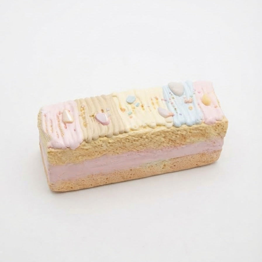 A rectangular sponge cake slice decorated with pastel pink, cream, and light blue frosting, topped with small decorative candies, on a plain white background.