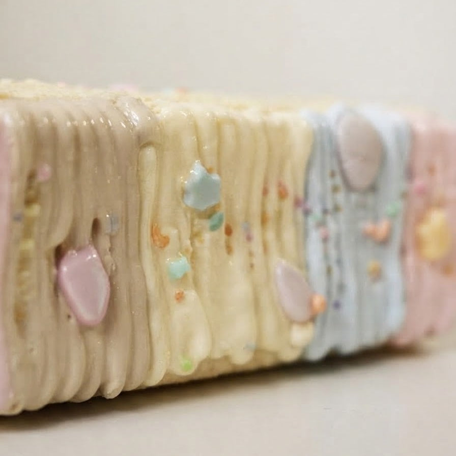 A close-up of a pastel-colored layered bar or cookie with cream, pink, and light blue sections, decorated with small candy hearts and sprinkles.