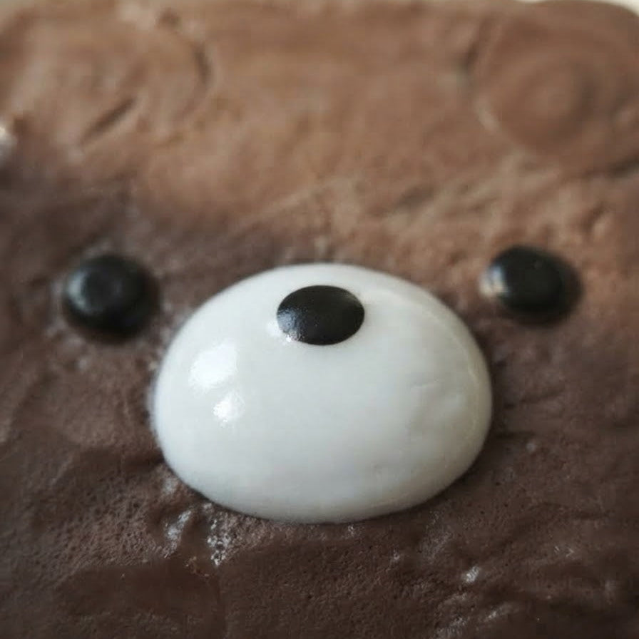 A close-up of a brown chocolate cake decorated with a white round face and two black candy eyes.