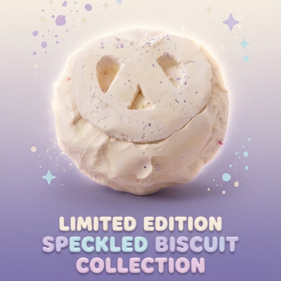 A single round baked good with a carved face design, shown on a soft gradient background with decorative sparkles and the text 'LIMITED EDITION SPECKLED BISCUIT COLLECTION' below.