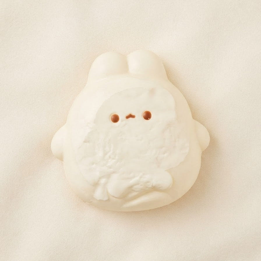 A small white plush bunny toy with a simple stitched face, photographed on a soft cream fabric background.