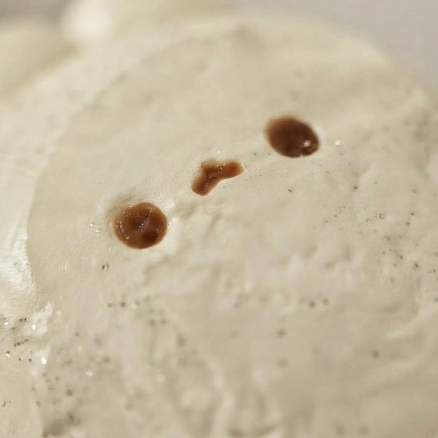 A close-up of a textured, off-white ceramic or stone object with three small brown spots resembling eyes or marks, set against a soft, neutral background.