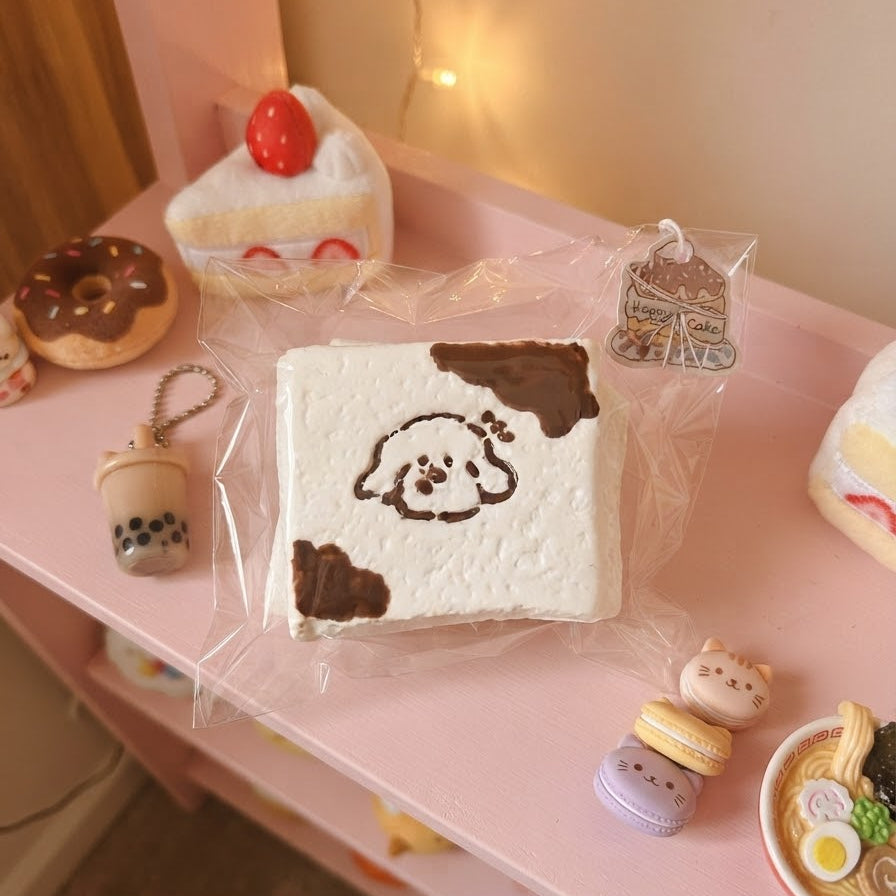 A square white squishy toy with a brown cow print and a cartoon face, still in its clear plastic packaging, displayed on a pink shelf alongside other cute food-themed squishies.