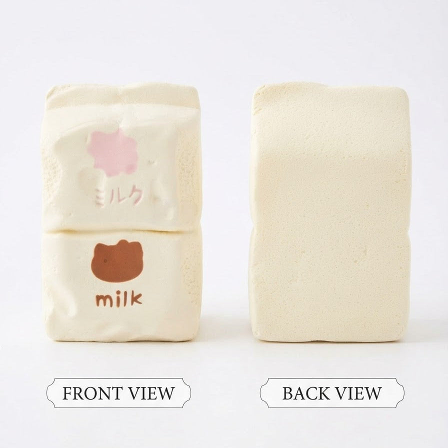 Two rectangular cream-colored bath blocks shown on a white background, labeled front view and back view. The left block has a pink flower and brown bear face graphic with the word 'milk' on it, while the right block is plain.