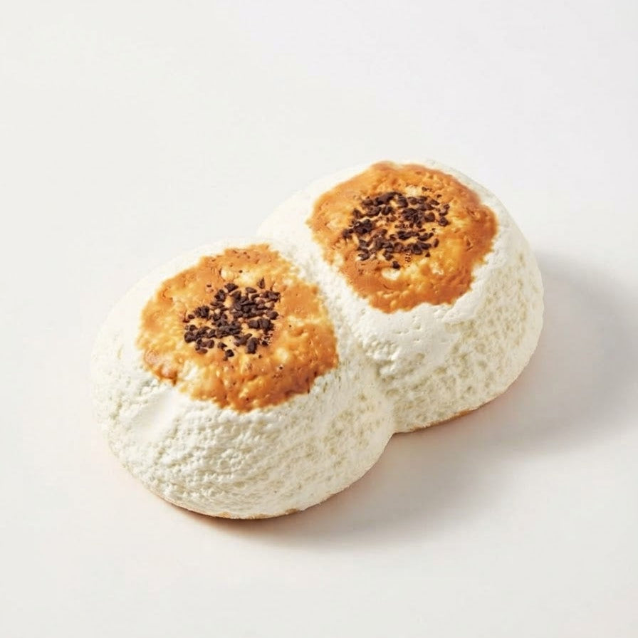 Two white, rounded pastries with golden-brown centers and dark sprinkles, photographed on a clean white background.