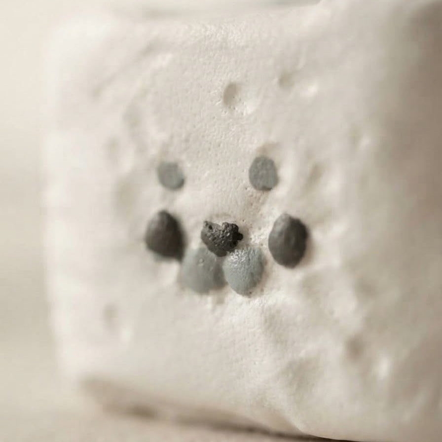 A close-up of a white textured rectangular object with a small gray and black face made of raised circular details, photographed on a soft beige background.