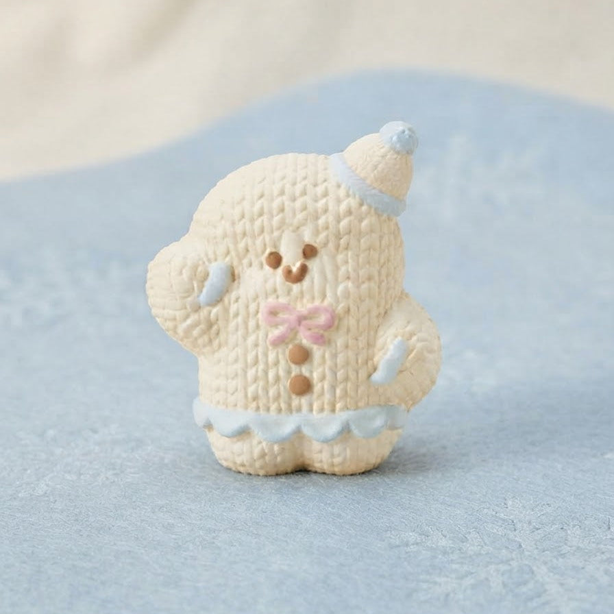 A small cream-colored knitted bear figurine wearing a light blue hat and skirt with a pink bow, standing on a textured light blue surface.