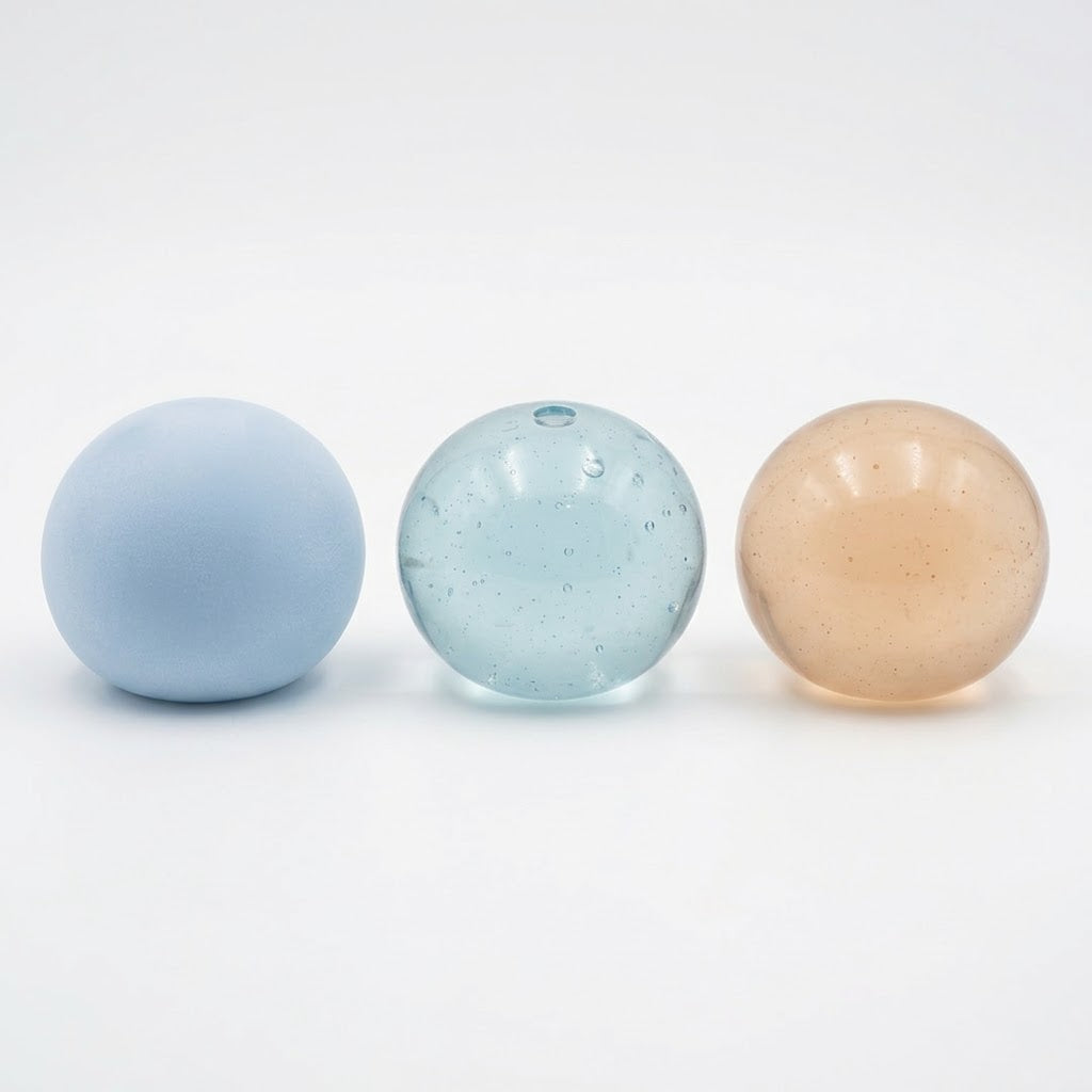 Three smooth decorative spheres in soft pastel colors on a clean white background: a matte light blue sphere on the left, a translucent light blue speckled sphere in the center, and a glossy peachy beige sphere on the right.