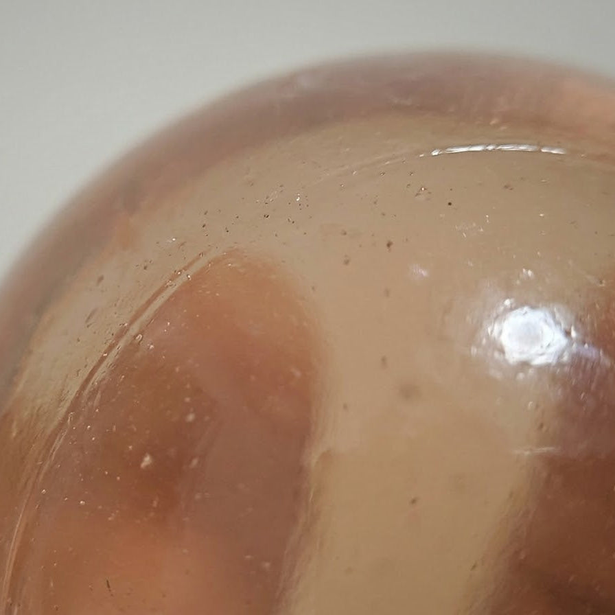 A close-up of a translucent peach-colored glass sphere with visible internal bubbles and a glossy reflective highlight, set against a plain light background.