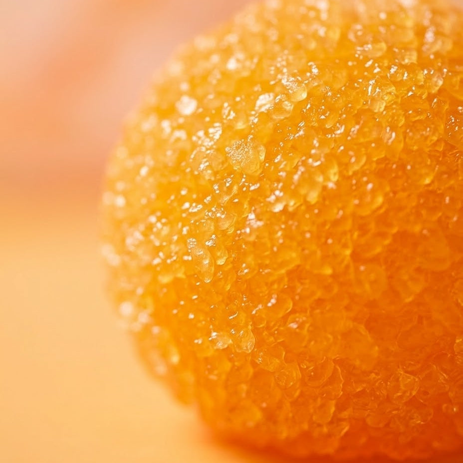 A close-up macro shot of a textured, translucent orange sphere, possibly a decorative crystal ball, sugar orb, or dried citrus peel piece, set against a matching warm orange background.