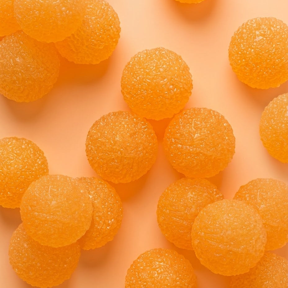 Orange sugar-coated round candies scattered on a peach-colored background.