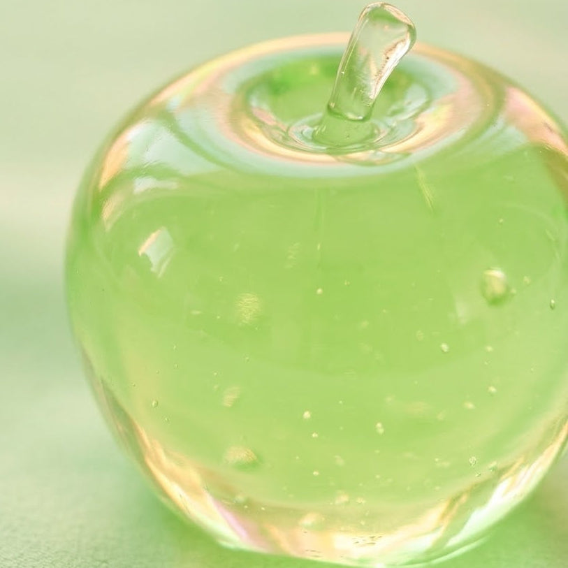 A translucent green apple-shaped decorative object with a small stem, photographed on a soft light green background.