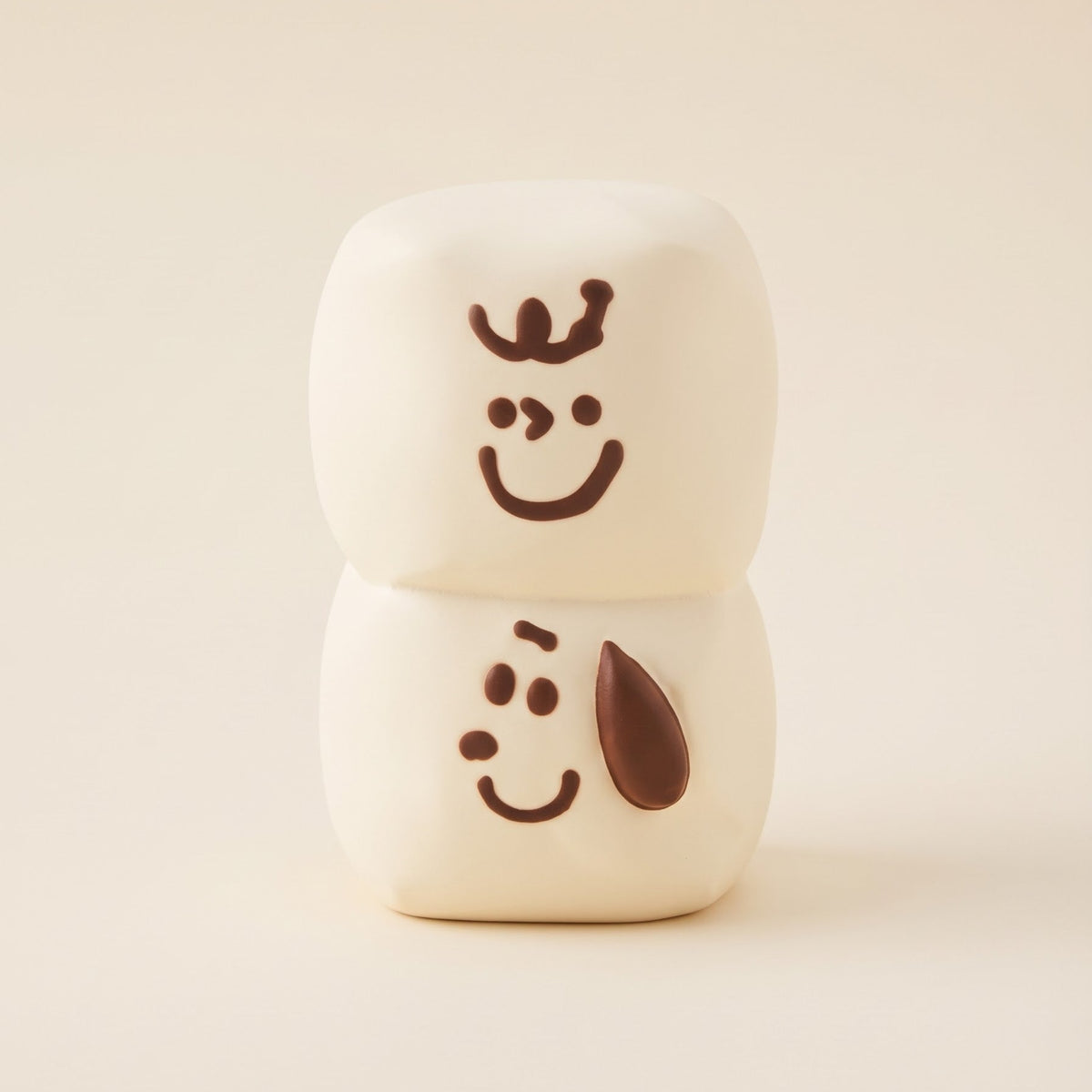 Two stacked cream-colored ceramic marshmallow figures with simple brown hand-drawn face details, set against a solid warm beige background.