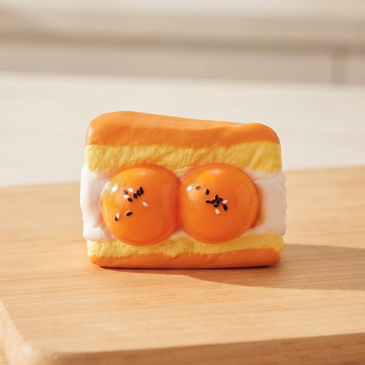 A novelty food-themed figurine shaped like a slice of toast with two orange egg yolks and white cream, sitting on a wooden cutting board.