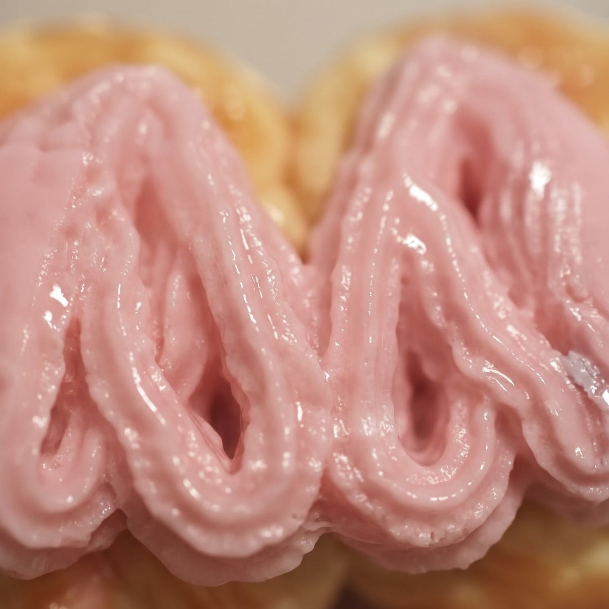 A close-up of a pastry or bread with thick, glossy pink frosting piped in wavy stripes over a golden-brown base.