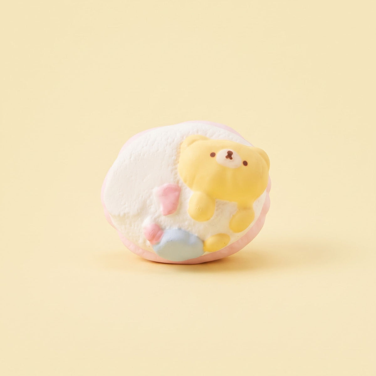 A cute, small pastel-colored plush toy or figurine featuring a yellow bear character peeking out from a white, fluffy shell-like body with pink and blue accents, set against a solid pale yellow background.