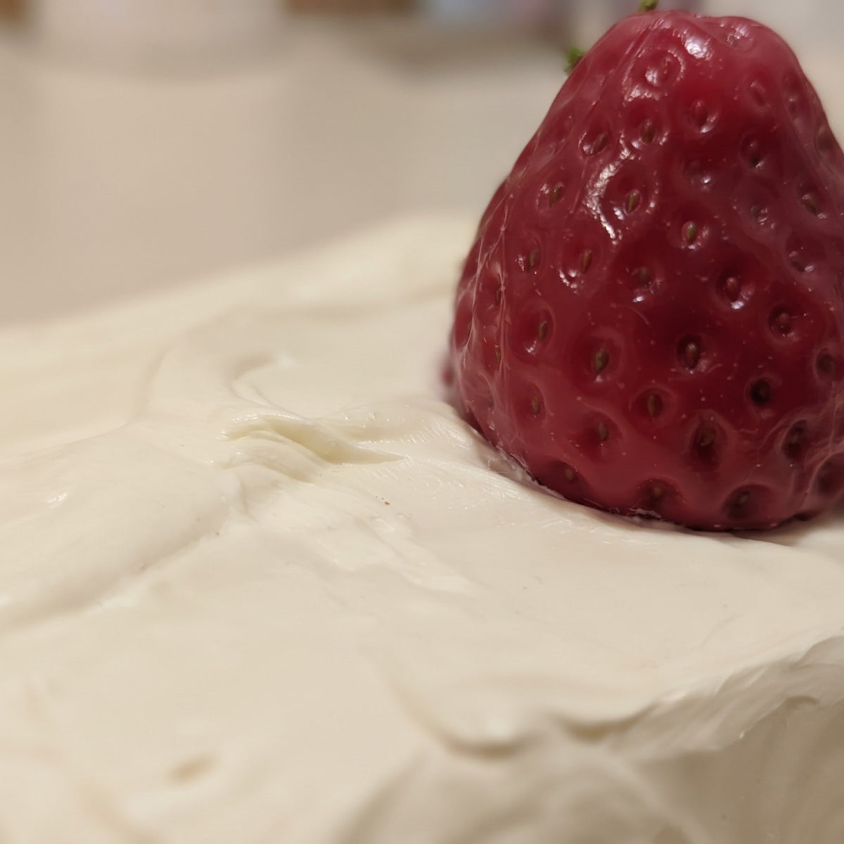 A close-up shot of a white cream-covered dessert or cake topped with a single fresh red strawberry.
