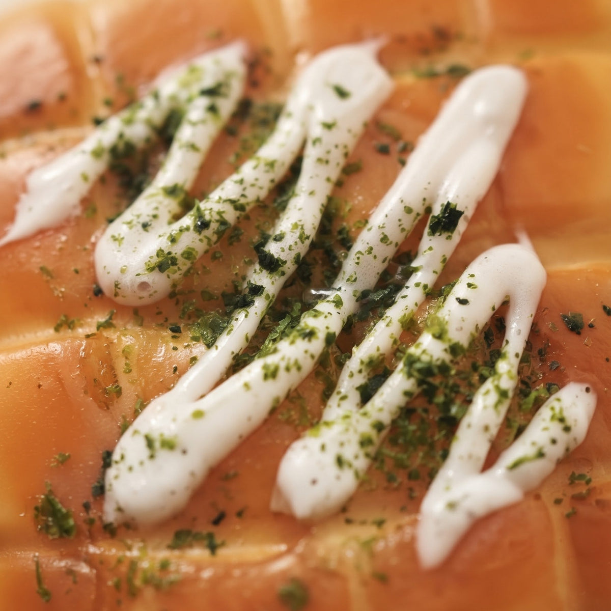 Close-up of a salmon fillet topped with white sauce and green herb seasoning, photographed in a clean food-style presentation.