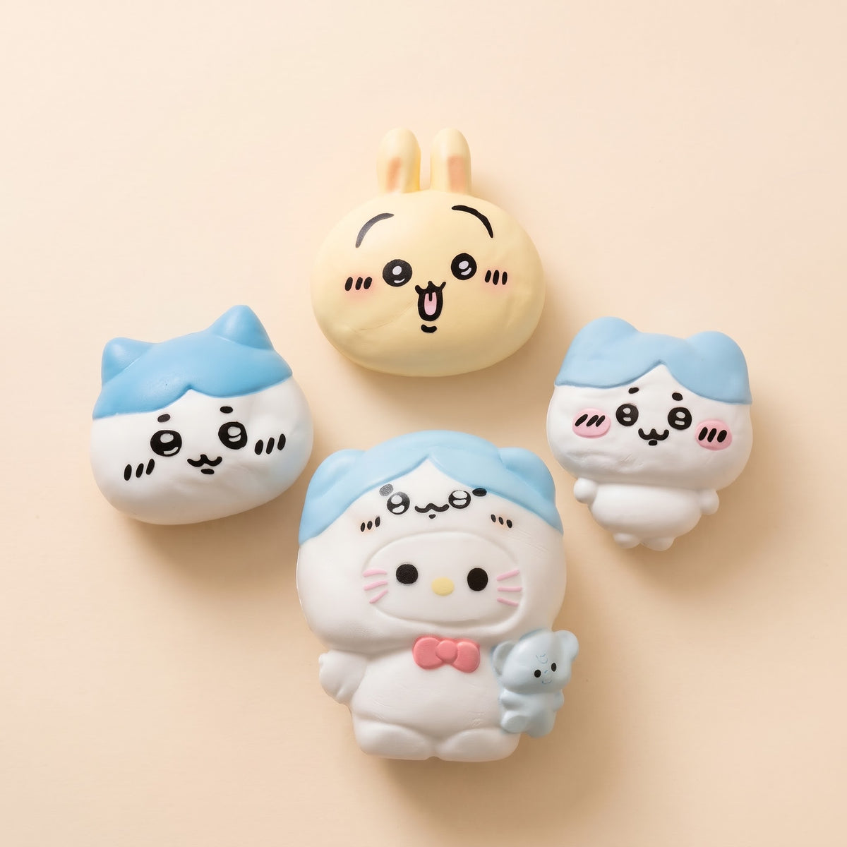 Four cute cartoon character plush toys arranged on a warm beige background. The characters have white and pastel blue bodies with simple black facial features and small pink accents.