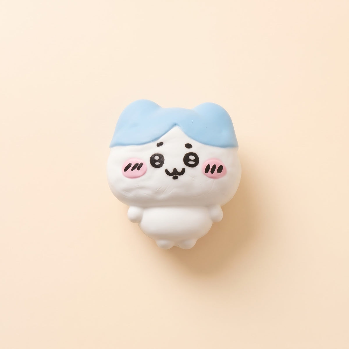 A cute, cartoonish white character figurine with light blue hair, black eyes, and pink cheeks, centered on a solid pale peach background.