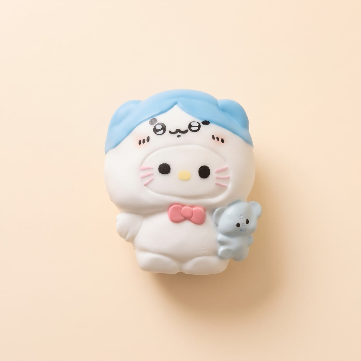 A cute, white cartoon character figurine wearing a light blue hat and holding a small light blue creature, set against a solid pale peach background.