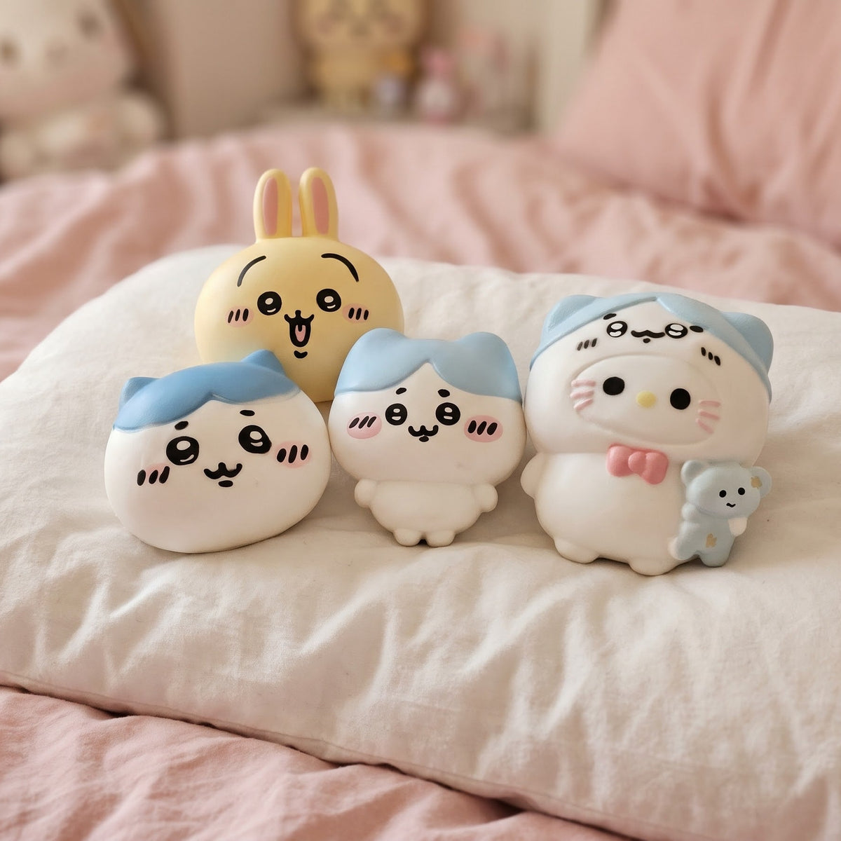 Four cute cartoon character plush toys arranged on a white pillow on a pink bed.