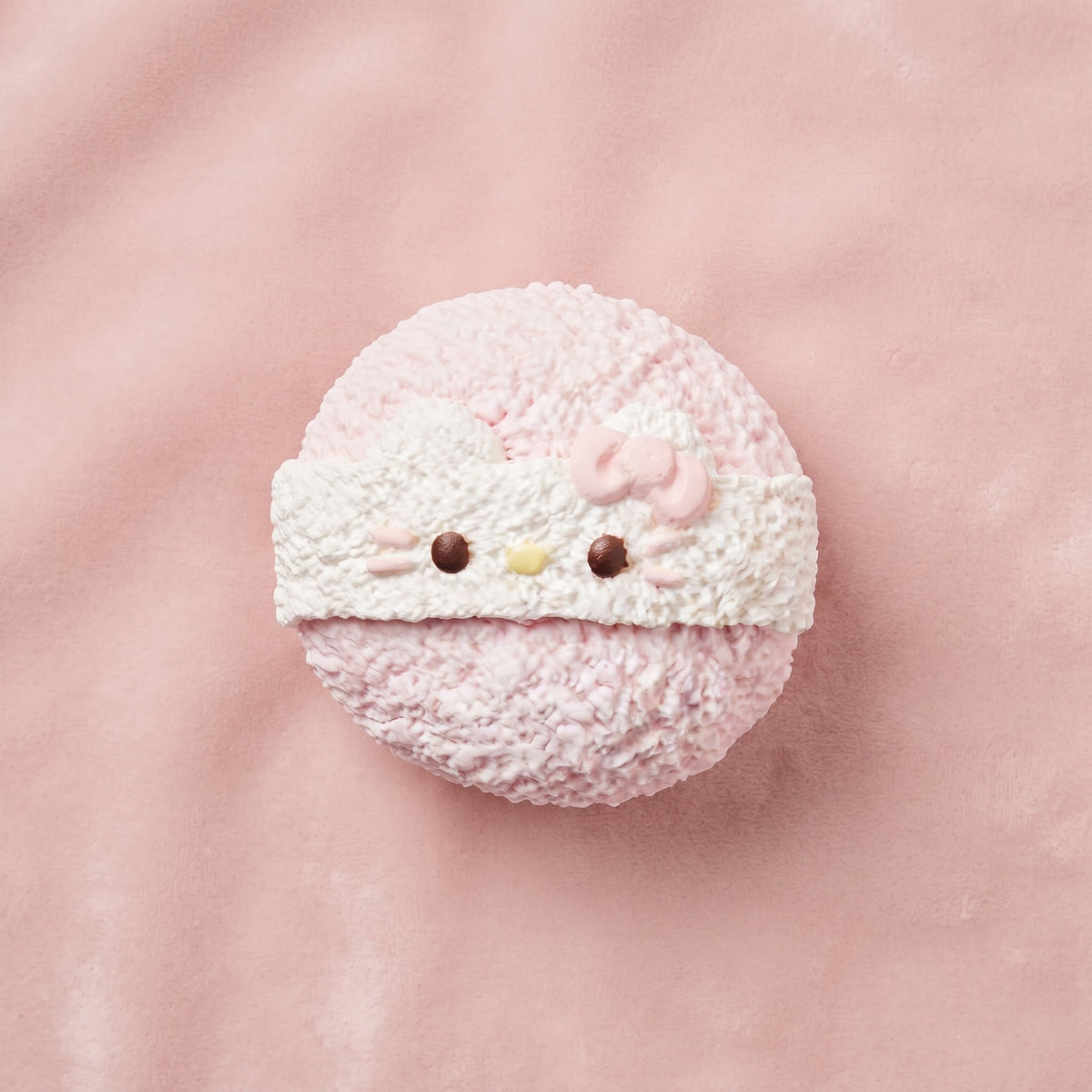 A pink and white textured Hello Kitty macaron-style treat on a soft pink background.