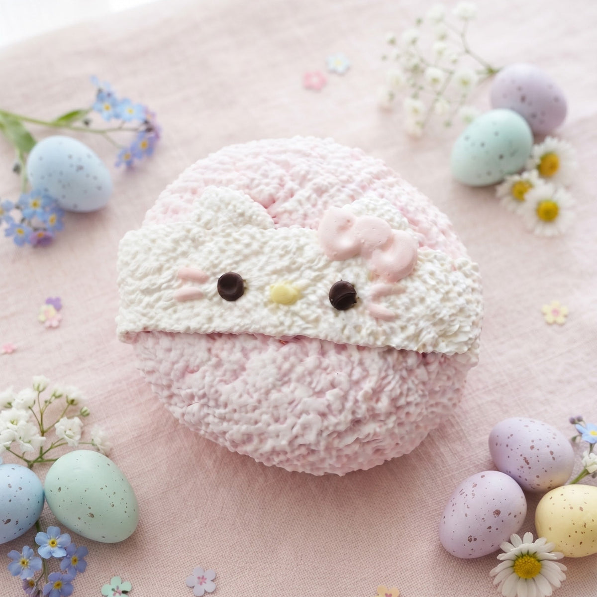 A round, textured pink and white plush pillow styled with pastel Easter eggs and small white flowers on a soft pink fabric background.