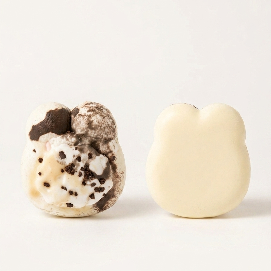 Two bear-shaped squishy toys on a plain white background: one with a cream and brown cookie-like pattern and one solid cream, with the text 'COOKIES & CREAM BEAR SQUISHY' below.