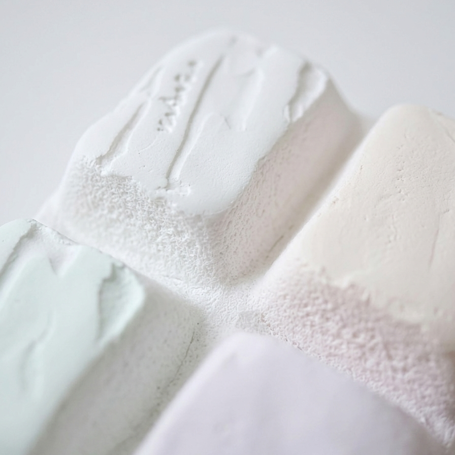 A close-up of textured, sculptural soap bars in soft pastel colors, including white, pale mint green, blush pink, and lavender, with one bar showing the embossed brand name 'sophia'.