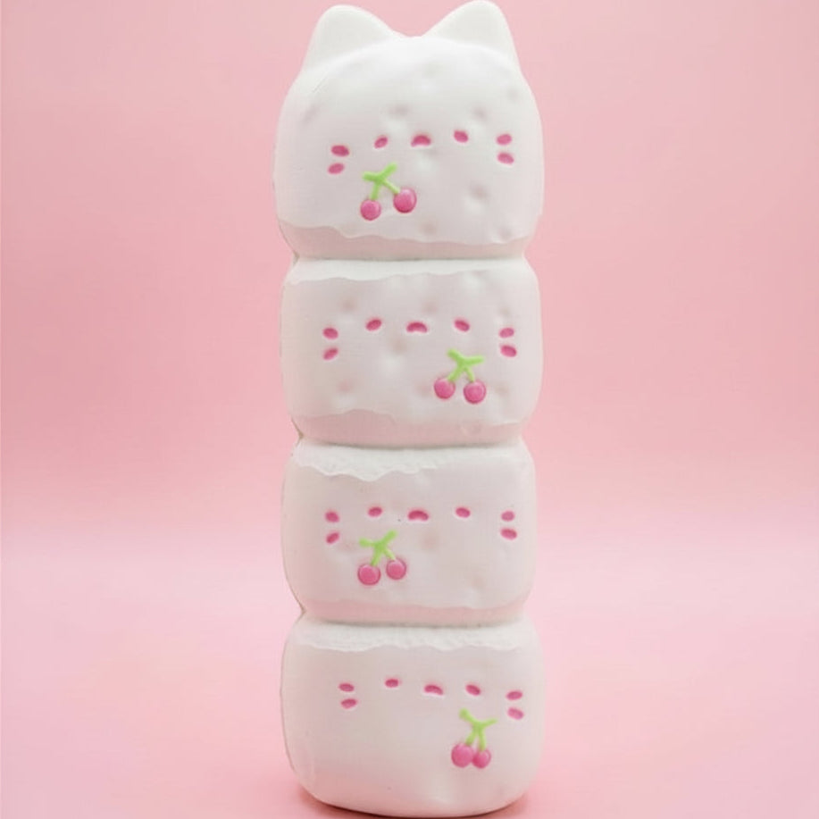 A stack of four white cat-shaped squishy toys with pink cherry details, set against a solid pink background.