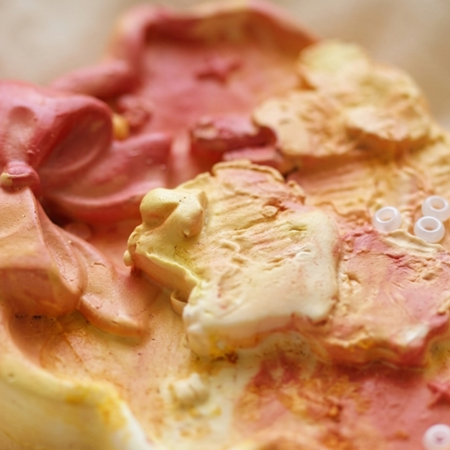 A close-up of a sculpted decorative object with a marbled pink, peach, and cream surface, photographed on a soft beige fabric background.