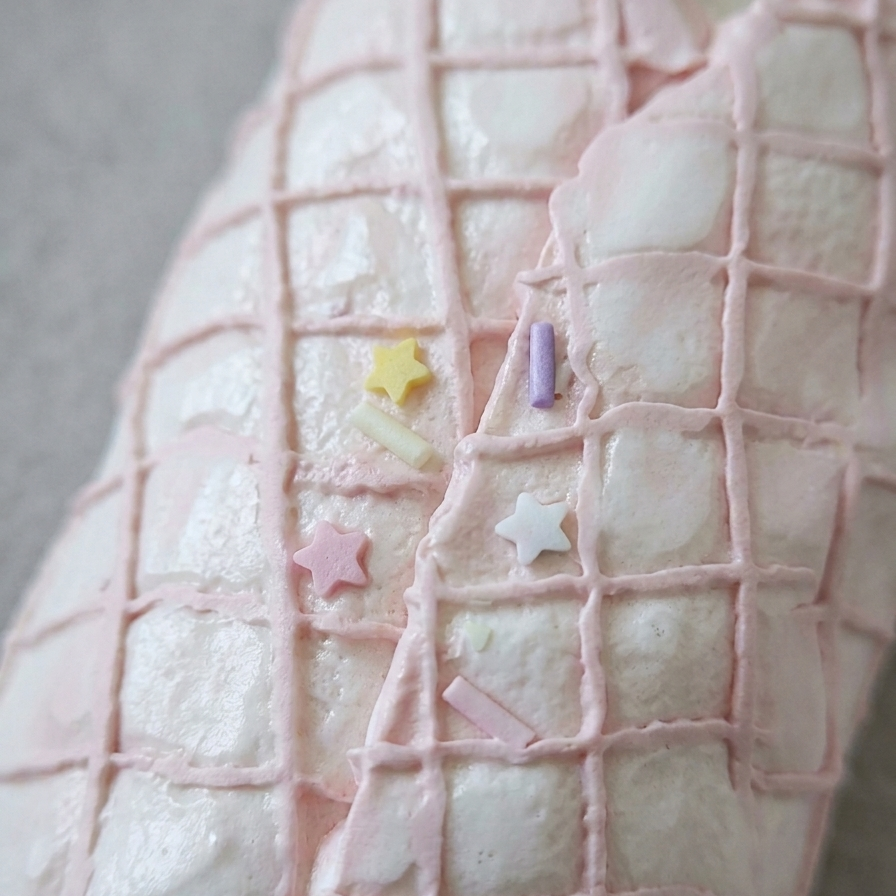 A close-up of a white textured surface with a light pink grid pattern and small pastel star and rectangular sprinkles in pink, yellow, and lavender.