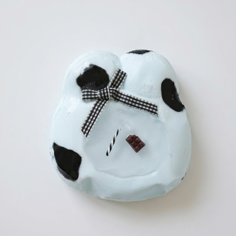 A light blue, cloud-shaped decorative plaque or wall hanging with black spots, a black-and-white checkered bow, and small facial details, photographed on a plain light background.