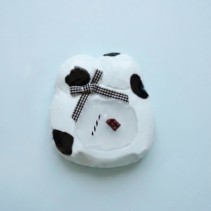 A white ceramic snowman ornament with black spots, a black-and-white checkered bow, and tiny facial details, photographed on a light blue background.