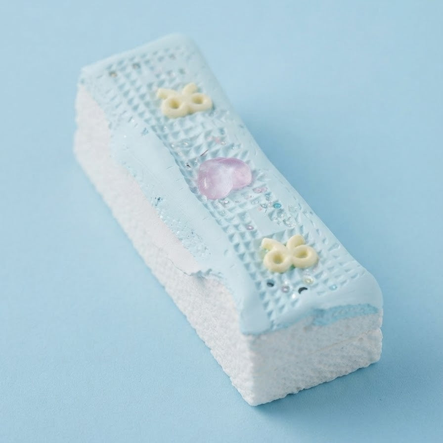 A rectangular white foam eraser with a light blue textured top surface, decorated with small yellow flower details and a pink heart, shown on a solid light blue background.