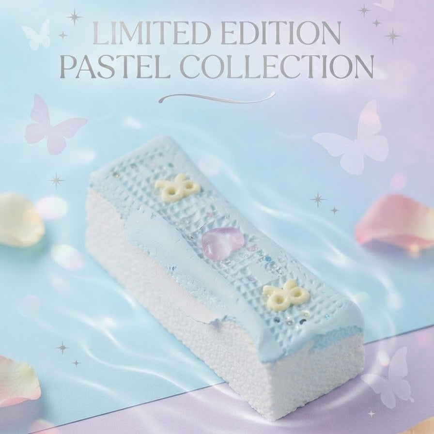 A rectangular pastel cake or pastry with light blue and white frosting, decorated with small yellow flower motifs and a pink heart, shown on a soft pastel background with butterflies, petals, and the text 'LIMITED EDITION PASTEL COLLECTION'.