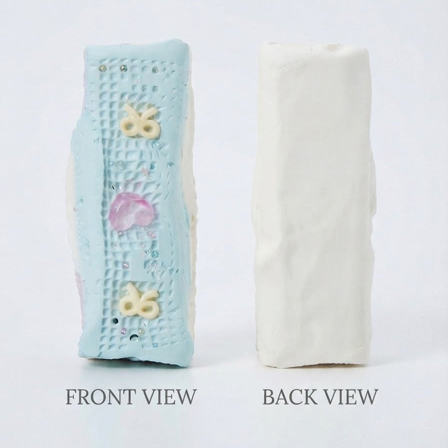 Two rectangular textured soap bars shown side by side on a white background, labeled FRONT VIEW and BACK VIEW. The left bar is light blue with small pastel butterfly and flower details, and the right bar is plain off-white.