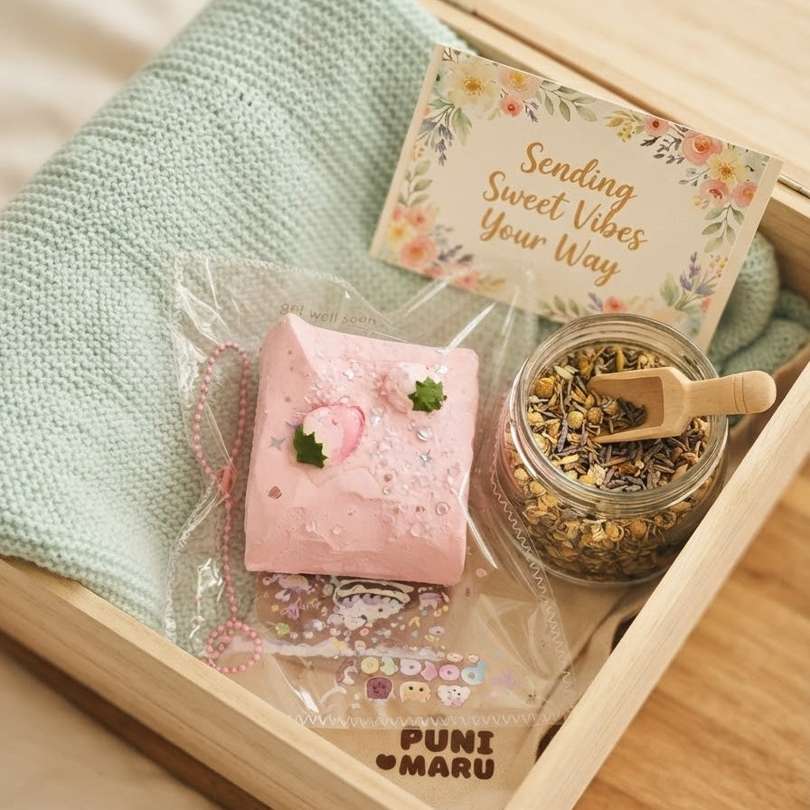 A wooden gift box containing a pink decorative soap in a clear bag, a small glass jar filled with dried botanicals and a wooden scoop, a folded mint green textured cloth, and a floral card that reads 'Sending Sweet Vibes Your Way.' The box is branded 'PUNI MARU.