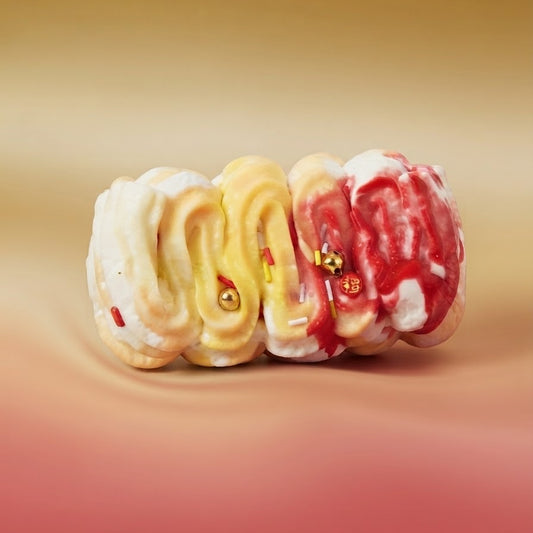 Three novelty ring toppers shaped like brains, featuring cream, yellow, and red swirled patterns with small gold ball accents, displayed on a smooth gradient background.