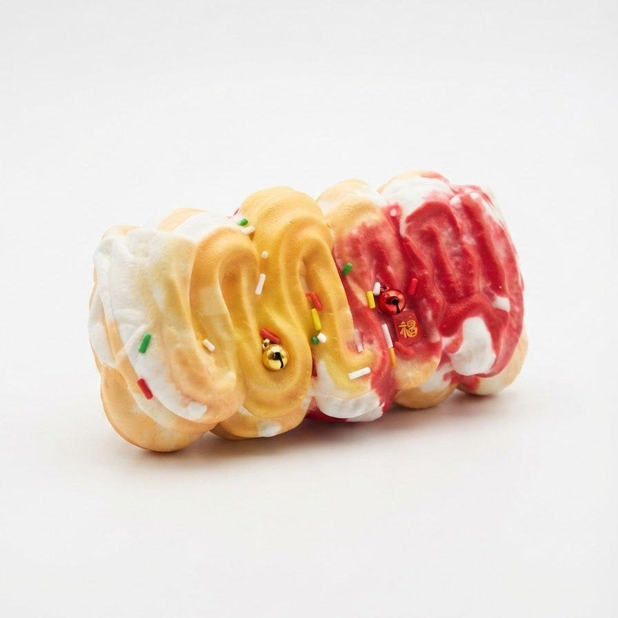 Three mini donut-shaped figurines with cream-colored frosting, golden-brown pastry swirls, and red icing drizzle, arranged in a row on a white background.
