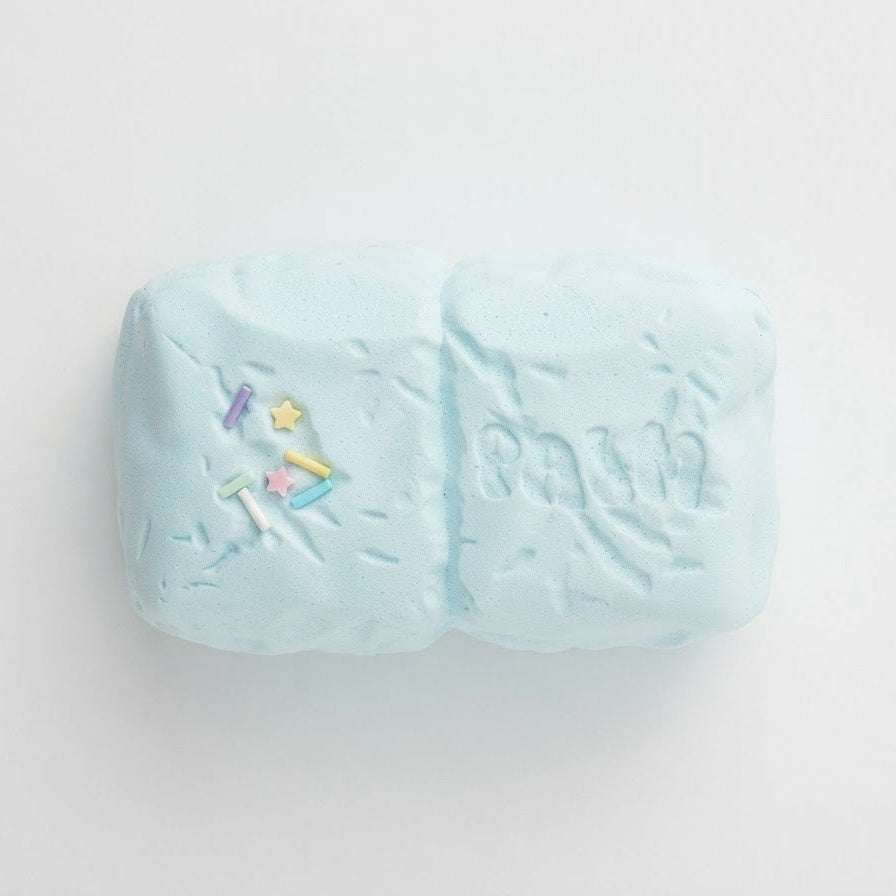 A light blue textured bath bomb with small multicolor star and triangle details near the bottom, photographed on a clean white background.