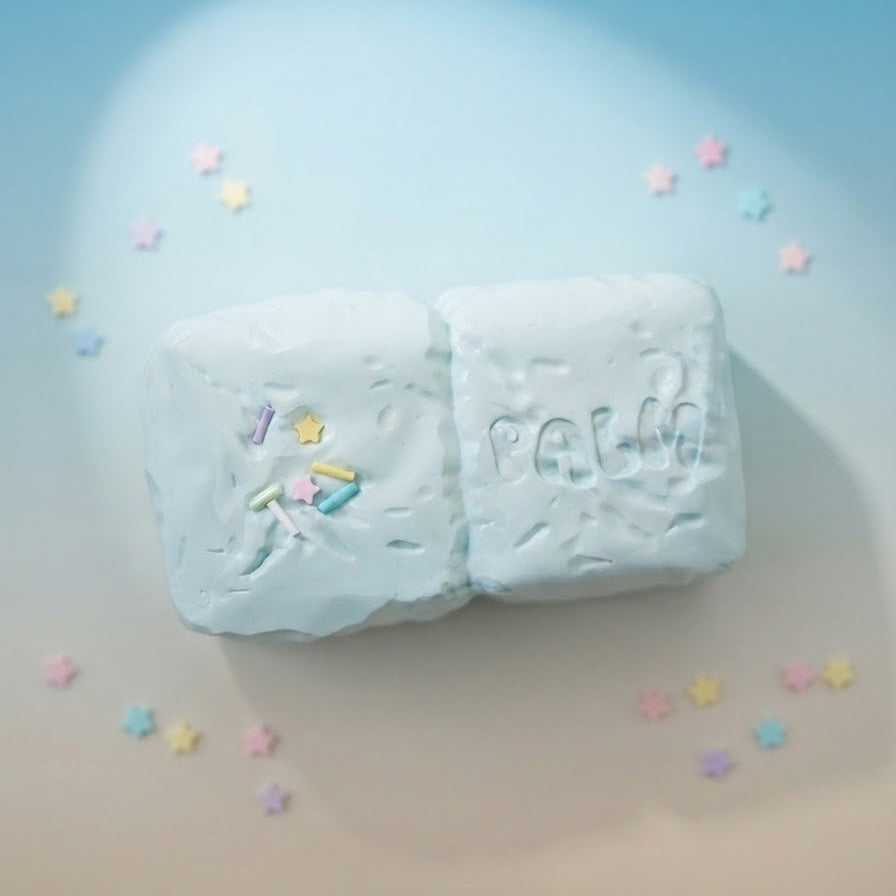 Two pale blue soap bars with pastel star sprinkles and embossed lettering, arranged on a soft blue-to-beige gradient surface with scattered pastel star confetti.