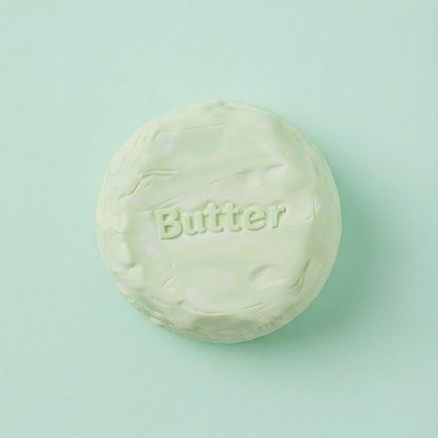 A round, pale mint green soap bar embossed with the word 'Butter' on its top face, centered on a solid mint green background.