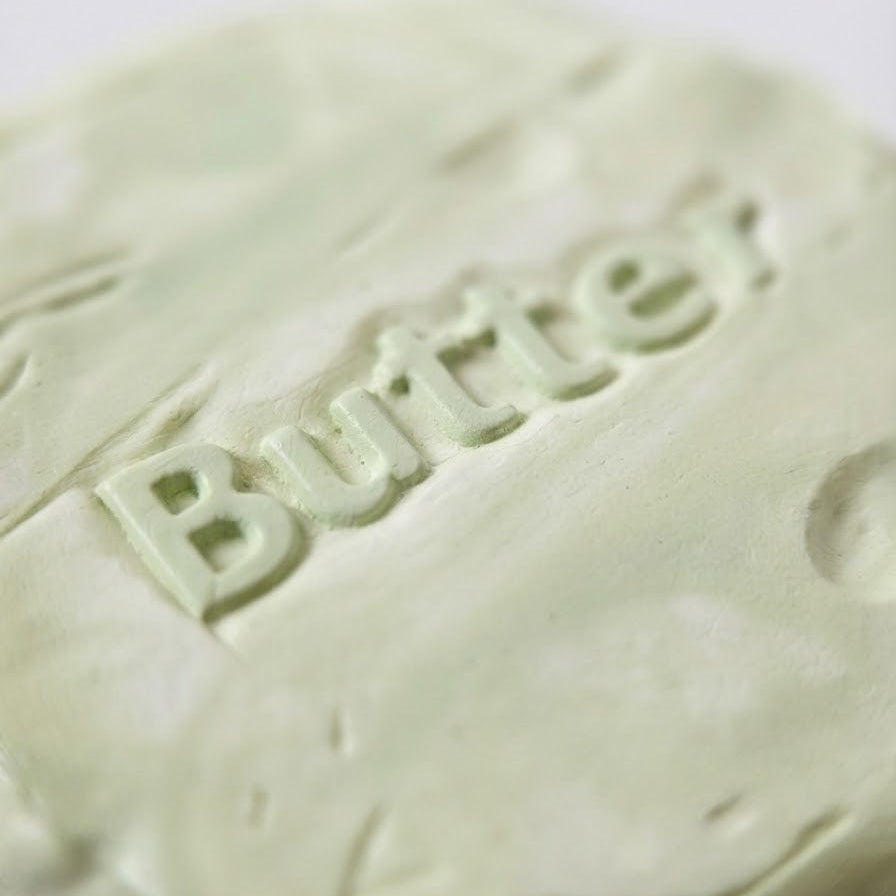 A close-up of a pale mint green bar of soap embossed with the word 'Butter'.